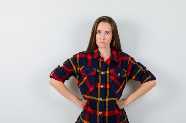 Free photo young lady holding hands on waist in casual shirt and looking spiteful. front view.