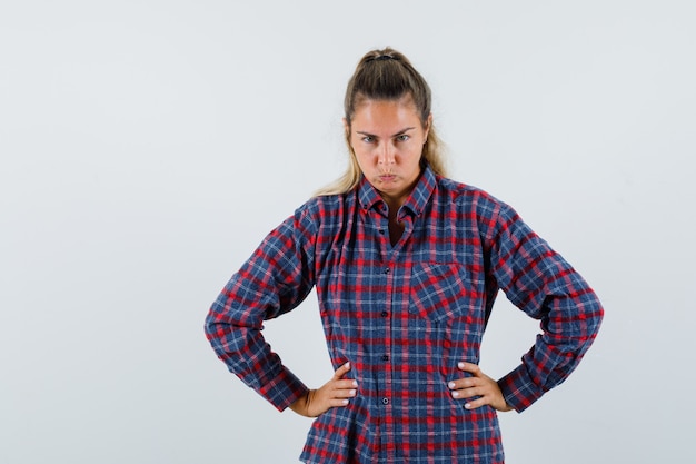 Free photo young lady holding hands on waist in checked shirt and looking pensive. front view.