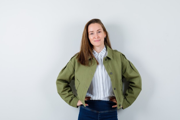 Young lady holding hands on waist in shirt, jacket and looking alluring , front view.