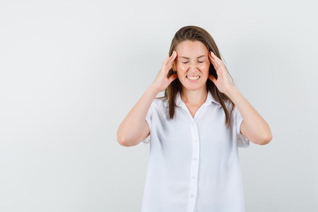 Young lady holding head in white blouse and looking uncomfortable