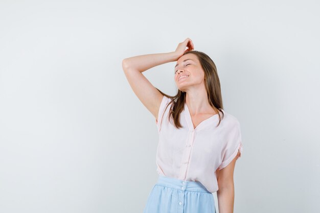 Young lady holding raised hand on head in t-shirt, skirt and looking hopeful , front view.