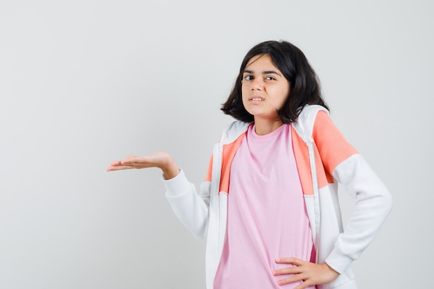 Free photo young lady in jacket, pink shirt spreading her palm aside, showing something and looking dissatisfied