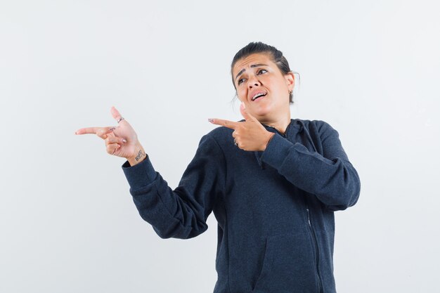 Young lady in jacket pointing aside and looking focused 