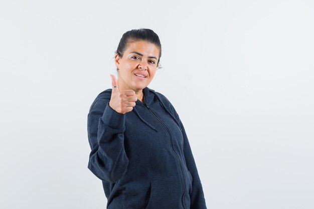 Young lady in jacket showing thumb up and looking glad 