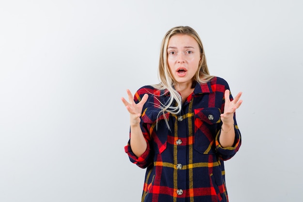 Free photo young lady keeping hands in aggressive manner in checked shirt and looking annoyed , front view.