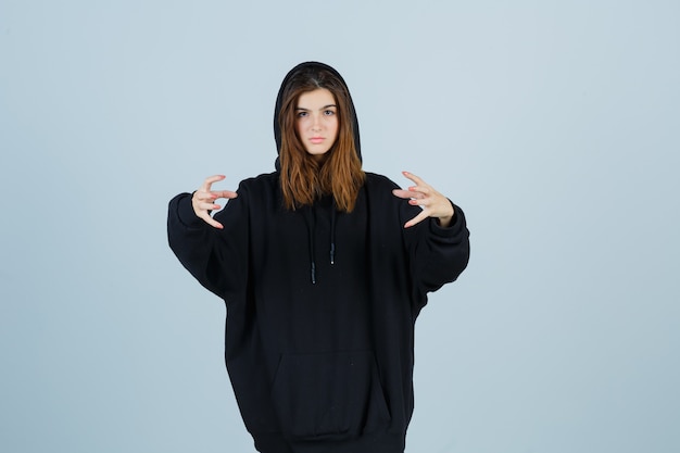 Free Photo young lady keeping hands in aggressive manner in oversized hoodie, pants and looking annoyed. front view.