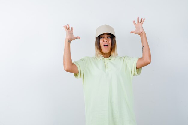 Young lady keeping hands in aggressive manner in t-shirt, cap and looking stressed , front view.