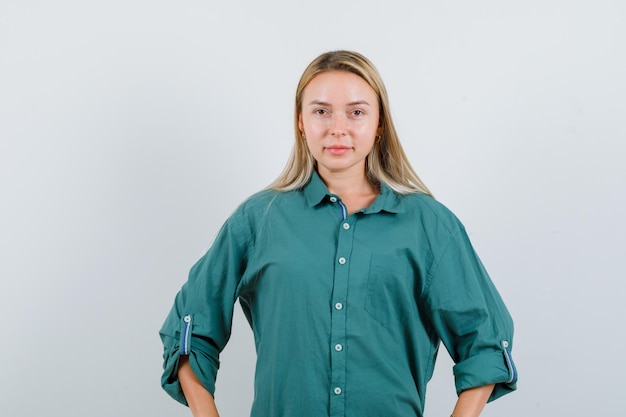 Young lady keeping hands on waist in green shirt and looking confident