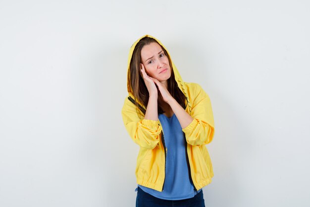 Young lady leaning cheek on palm in t-shirt, jacket and looking sad. front view.