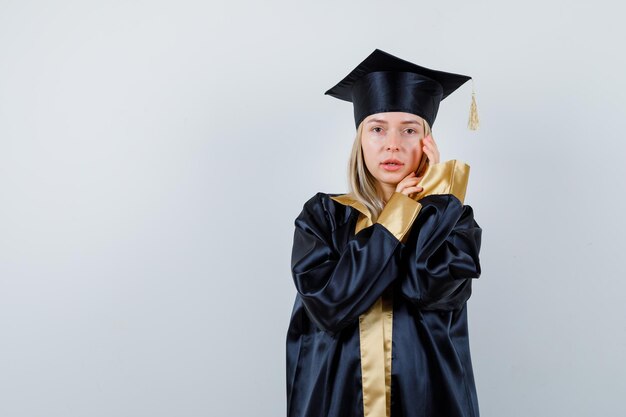 Young lady looking at camera while posing in academic dress and looking worried.