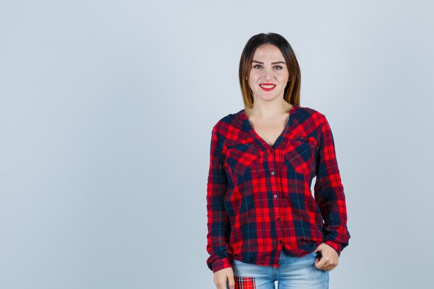 Young lady looking at front in checked shirt and looking cheerful. front view.