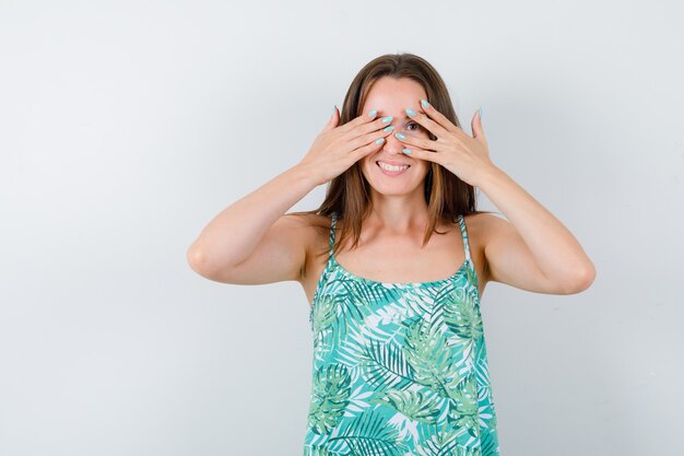 Young lady looking through fingers in blouse and looking cute , front view.