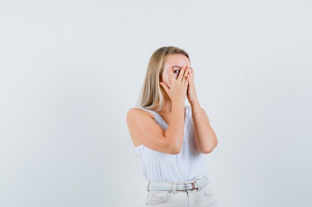 Young lady looking through fingers in white blouse and looking excited