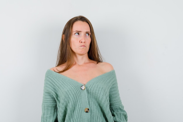 Young lady looking up while thinking in wool cardigan and looking troubled , front view.