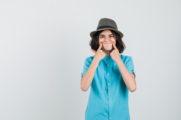 Young lady making fake smile with her fingers in blue shirt and looking positive