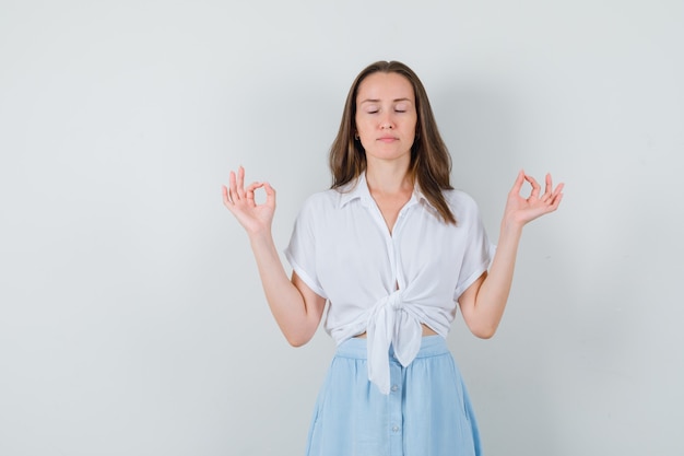 Young lady meditating in blouse, skirt and looking calm