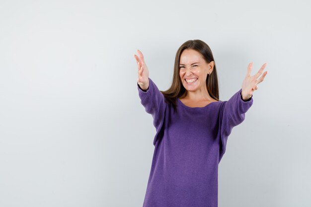 Young lady opening arms for hug in violet shirt and looking happy. front view.