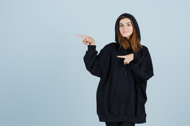 Young lady in oversized hoodie, pants pointing to the left side and looking confident , front view.