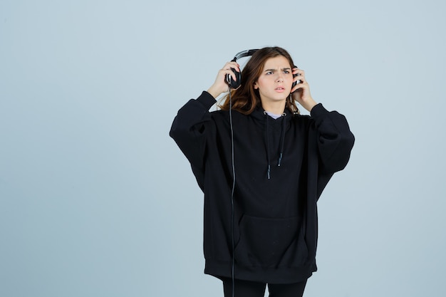 Free photo young lady in oversized hoodie, pants taking of handphones and looking puzzled , front view.