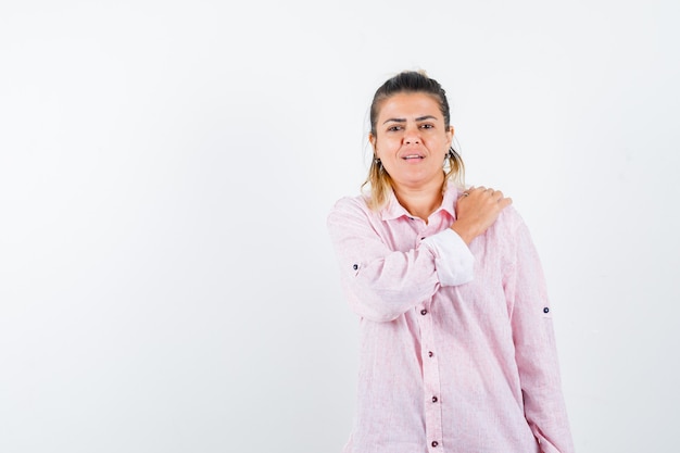 Young lady in pink shirt keeping hand on shoulder and looking pensive 