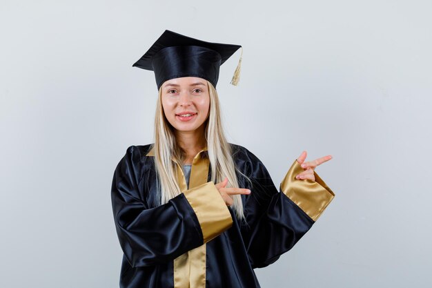 Young lady pointing aside in academic dress and looking alluring