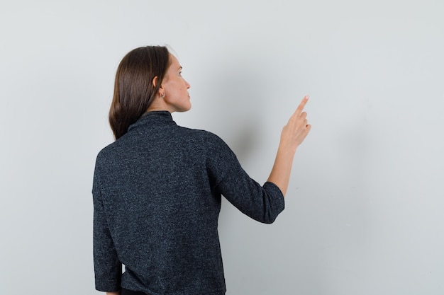 Free Photo young lady pointing away in shirt and looking pensive , back view