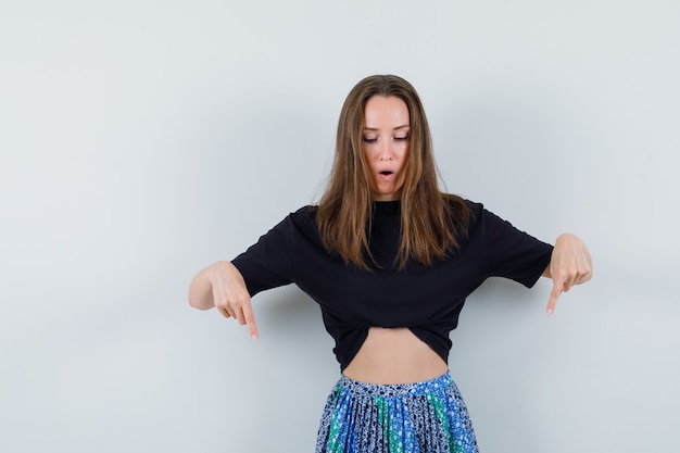 Free photo young lady pointing down in blouse, skirt and looking focused