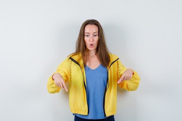 Young lady pointing down in t-shirt and looking amazed. front view.