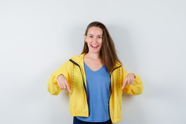 Young lady pointing down in t-shirt and looking cheerful , front view.