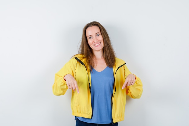 Young lady pointing down in t-shirt and looking hopeful , front view.