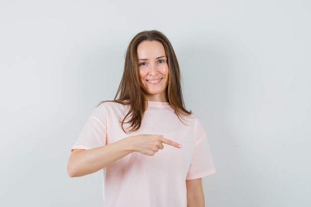 Young lady pointing finger down in pink t-shirt and looking joyful  