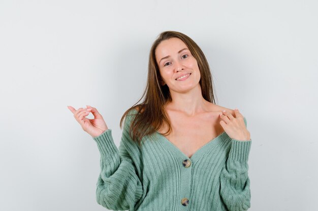 Young lady pointing left in wool cardigan and looking cheerful. front view.