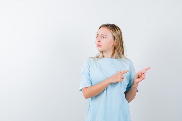 Young lady pointing to the right side in t-shirt and looking hesitant , front view.