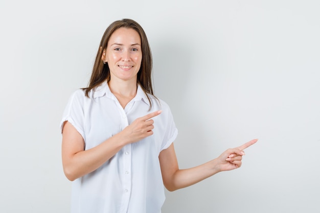 Young lady pointing to the side in white blouse and looking optimistic.