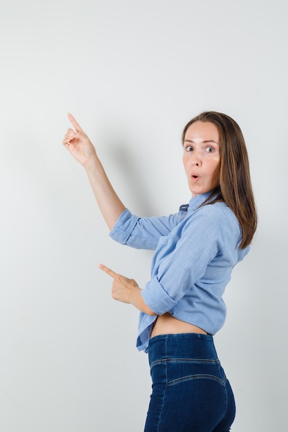 Young lady pointing up in blue shirt, pants and looking surprised.