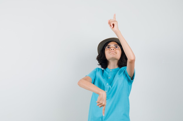 Young lady pointing up and down in blue shirt, hat and looking concentrated.