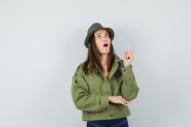 Young lady pointing up in jacket pants hat and looking amazed 