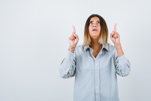 Young lady pointing up in oversized shirt and looking confident , front view.