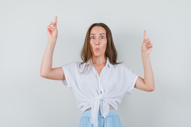 Young lady pointing up while pouting her lips in blouse and skirt and looking concentrated