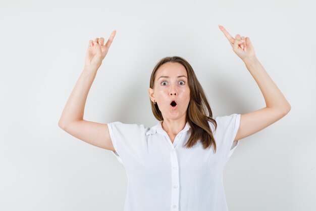 Young lady pointing to up in white blouse and looking amazed