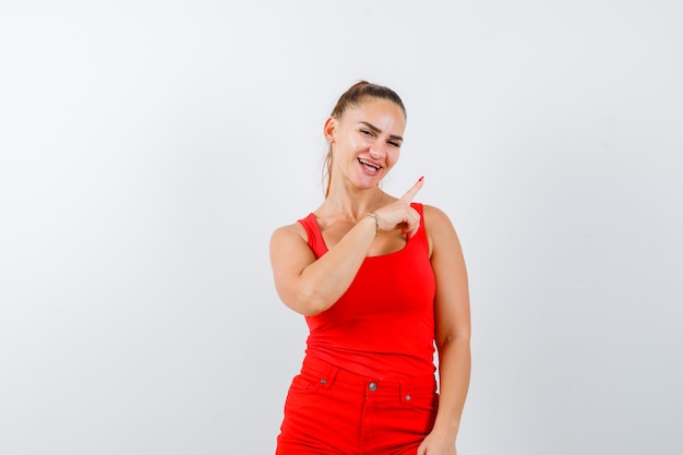 Young lady pointing at upper right corner in red singlet, red trousers and looking cheery. front view.