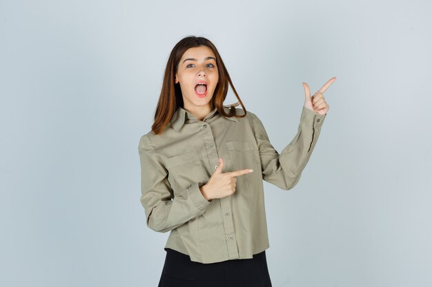 Young lady pointing at upper right corner in shirt, skirt and looking happy. front view.