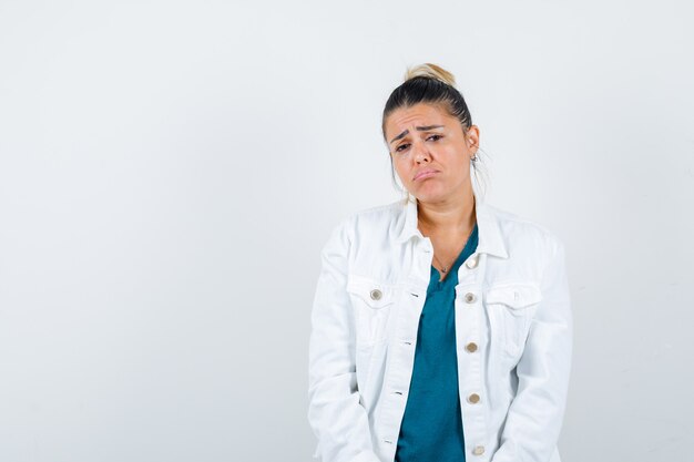 Young lady posing while in shirt, white jacket and looking disappointed , front view.