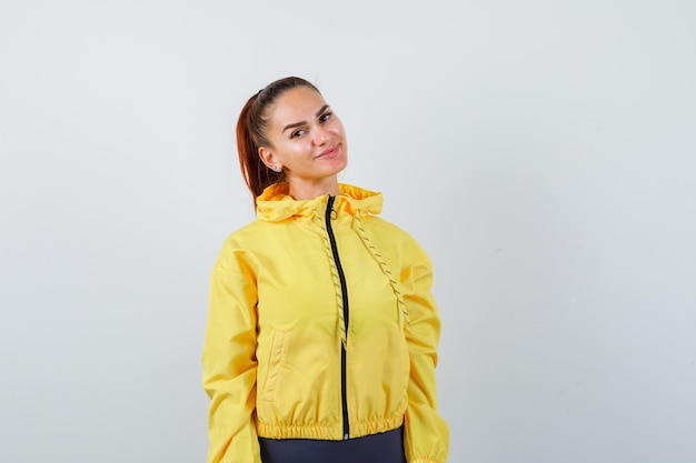 Young lady posing in yellow jacket and looking pleased. front view.