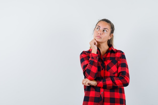 Young lady propping chin on fist in checked shirt and looking pensive