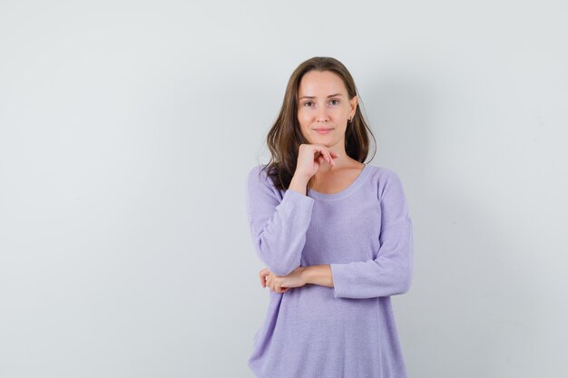 Young lady propping chin on hand in casual shirt and looking sensible 