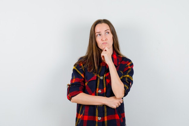 Free photo young lady propping chin on hand in casual shirt and looking thoughtful , front view.