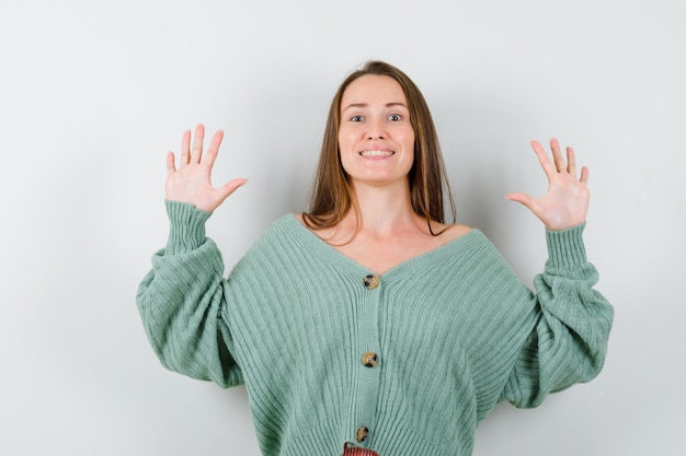 Free Photo young lady raising hands in surrender gesture in wool cardigan and looking happy. front view.