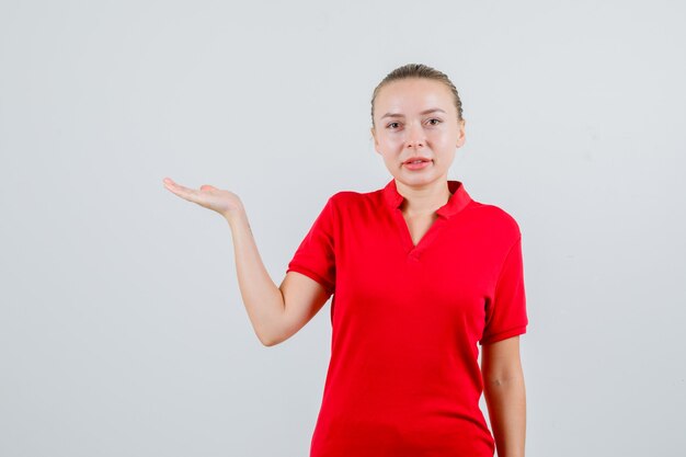 Young lady raising palm as catching something in red t-shirt and looking cheerful