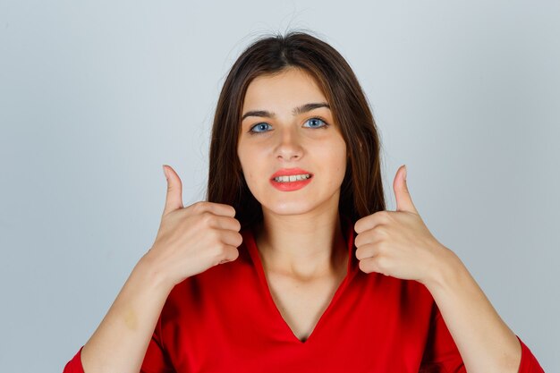 Young lady in red blouse showing thumbs up and looking glad